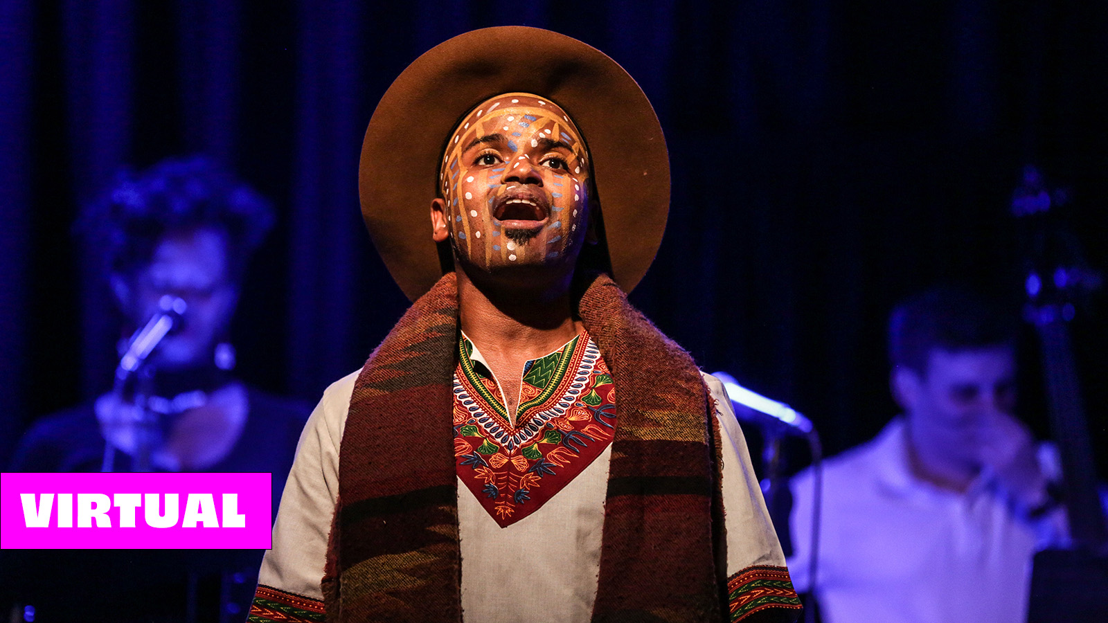 Alphonso Horne is wearing a brown hat, scarf, and embroidered shirt with face paint on while singing onstage