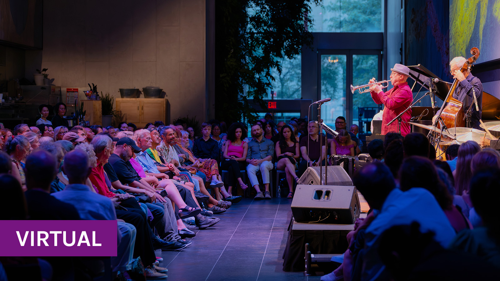 A dimly-lit audience watches a trumpet player and upright bassist perform onstage at the David Rubenstein Atrium. 