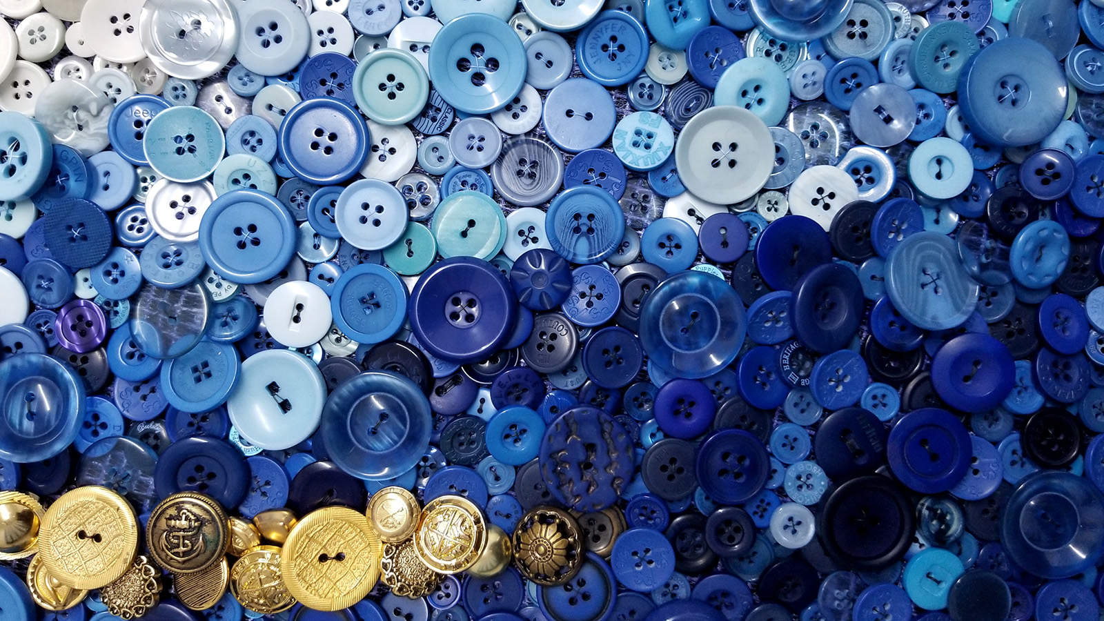 Circular buttons of various sizes in a descending blue gradient from white to navy. In the bottom lefthand corner is a clump of gilded golden circular buttons in various vintage styles