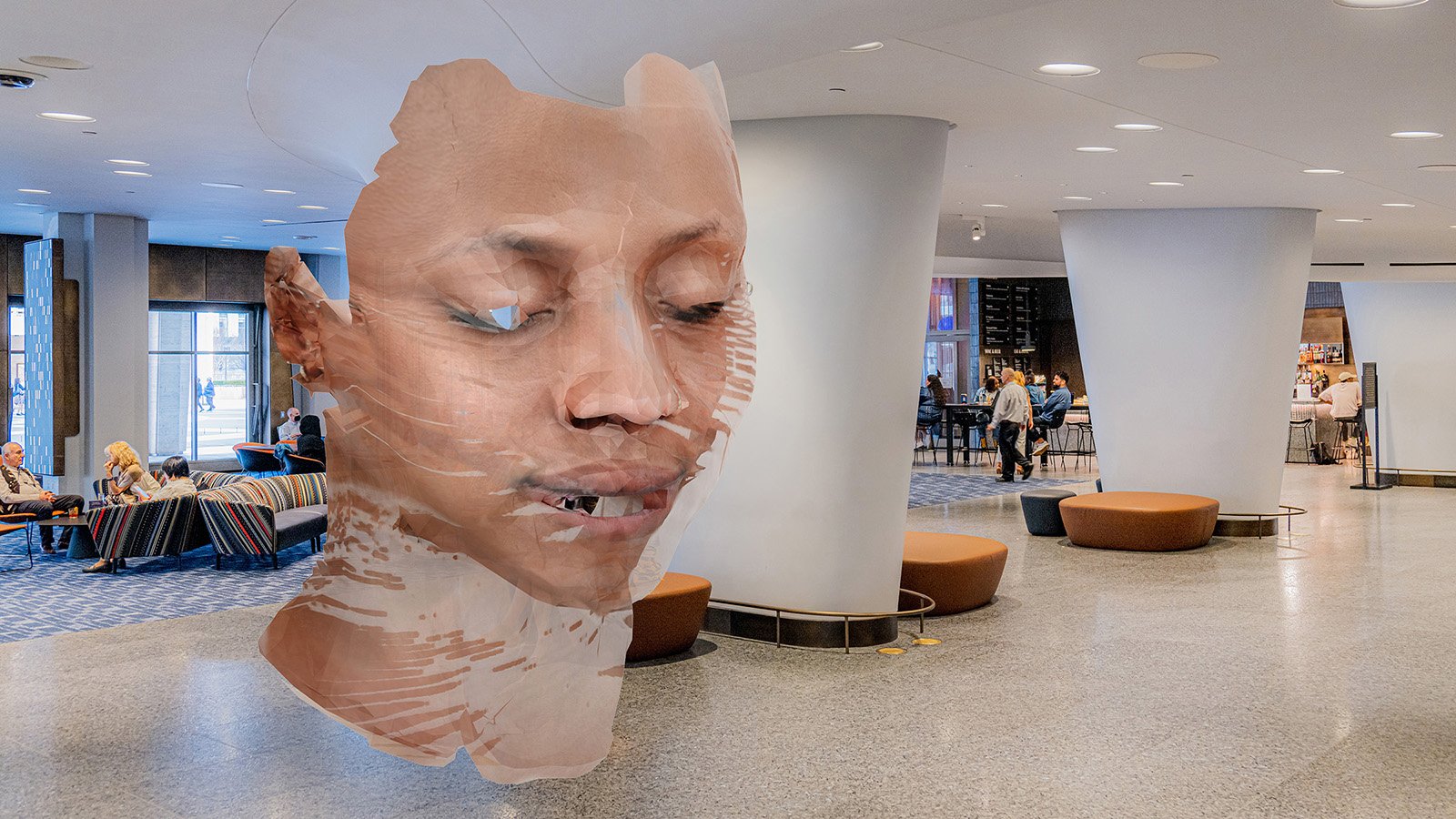 A photo of the lobby of David Geffen Hall with a floor-to-ceiling augmented reality bust of a distorted face composed of light skin tones in the center.