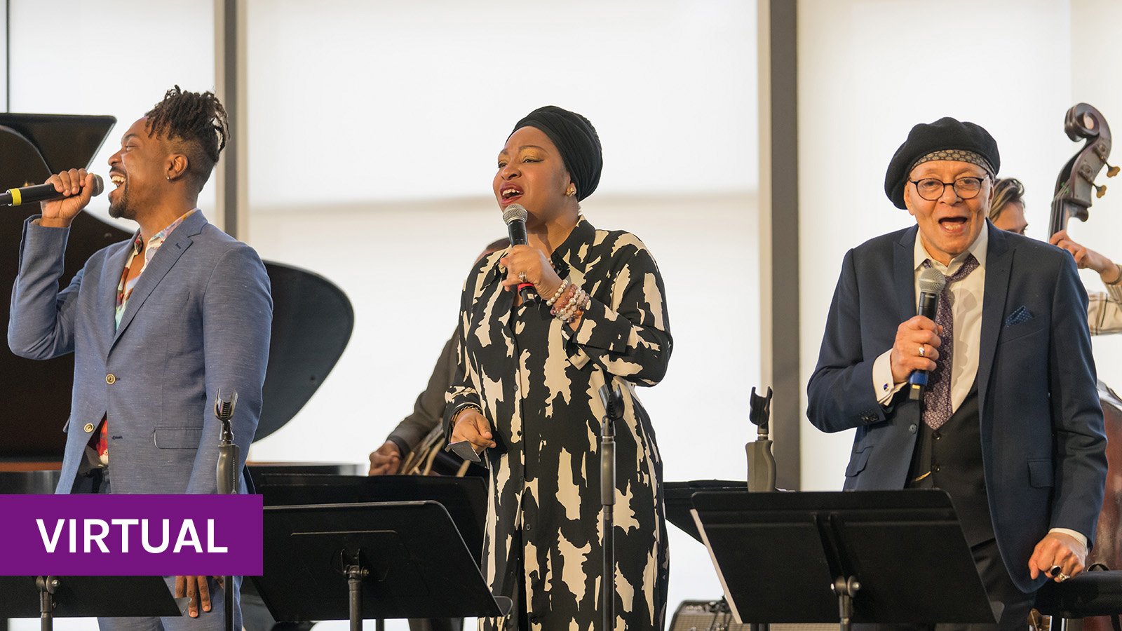 Three smartly dressed singers on a warmly lit stage hold microphones and smile, mid-song.