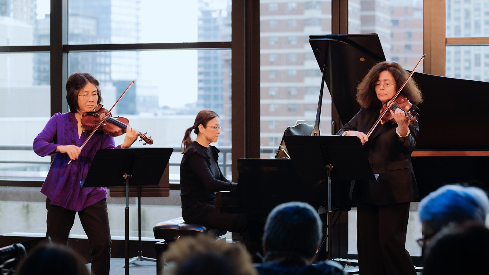 A dimly-lit audience watches a trumpet player and upright bassist perform onstage at the David Rubenstein Atrium. 