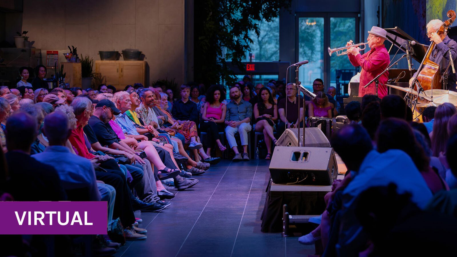 A dimly-lit audience watches a trumpet player and upright bassist perform onstage at the David Rubenstein Atrium. 