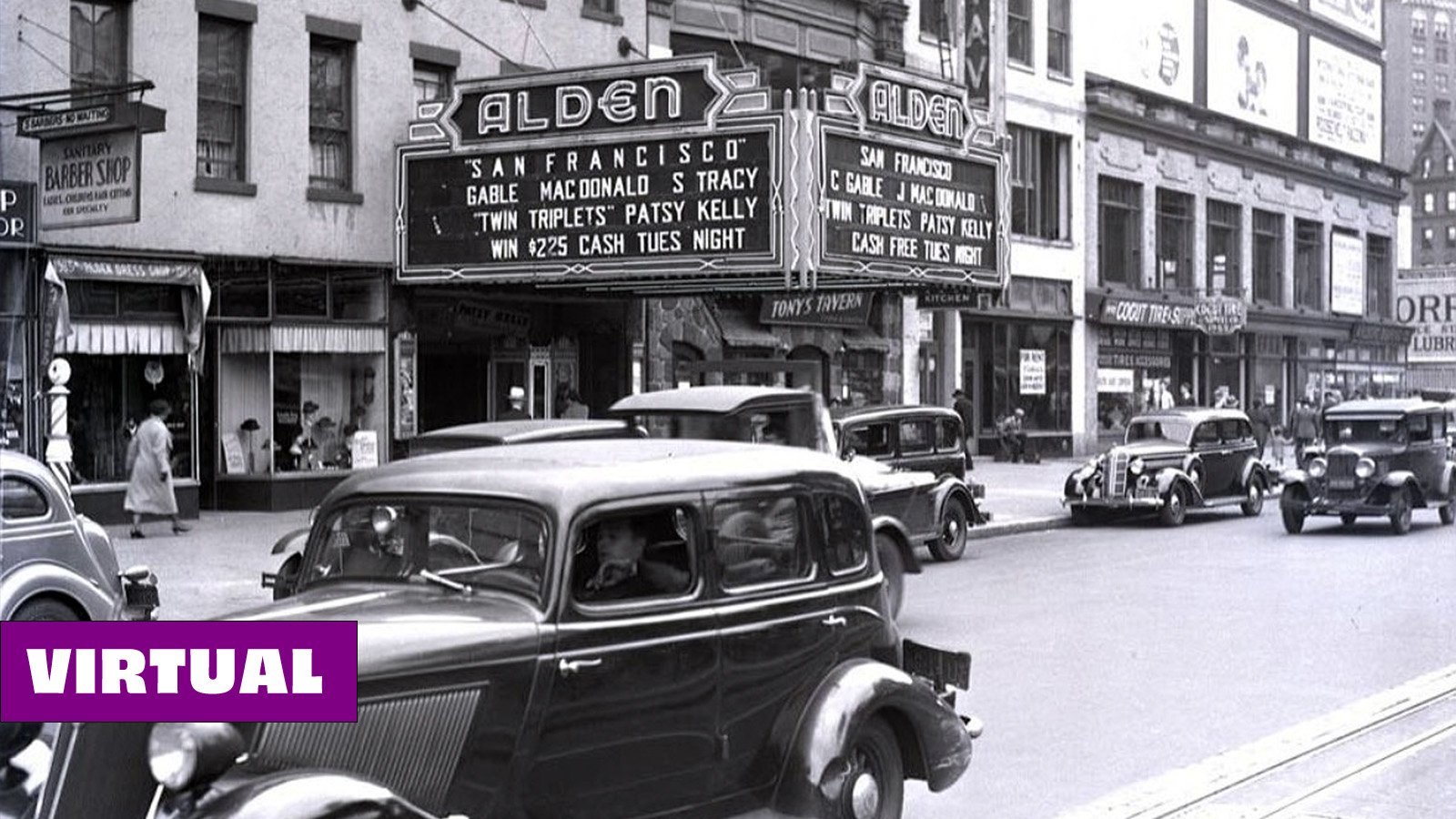 A black and white image of a city block with old-fashioned cars and pedestrians. In the background, a movie theater marquis reads: Alden. 'San Francisco' Gable Macdonald, S Tracy. 'Twin Triplets' Patsy Kelly. Win $225 Cash Tues Night